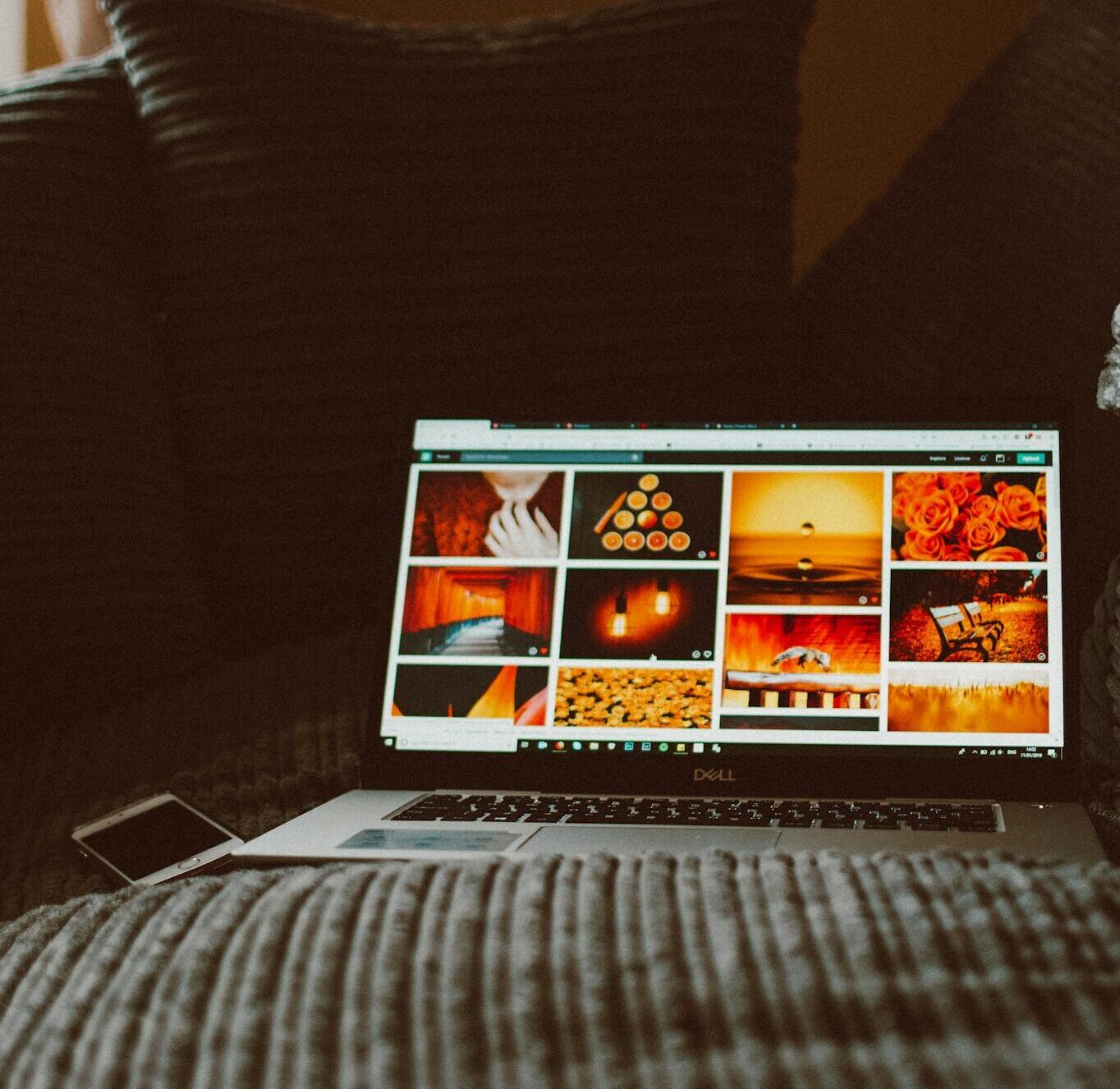 Laptop displaying photos surrounded by pillows, creating a cozy indoor environment.